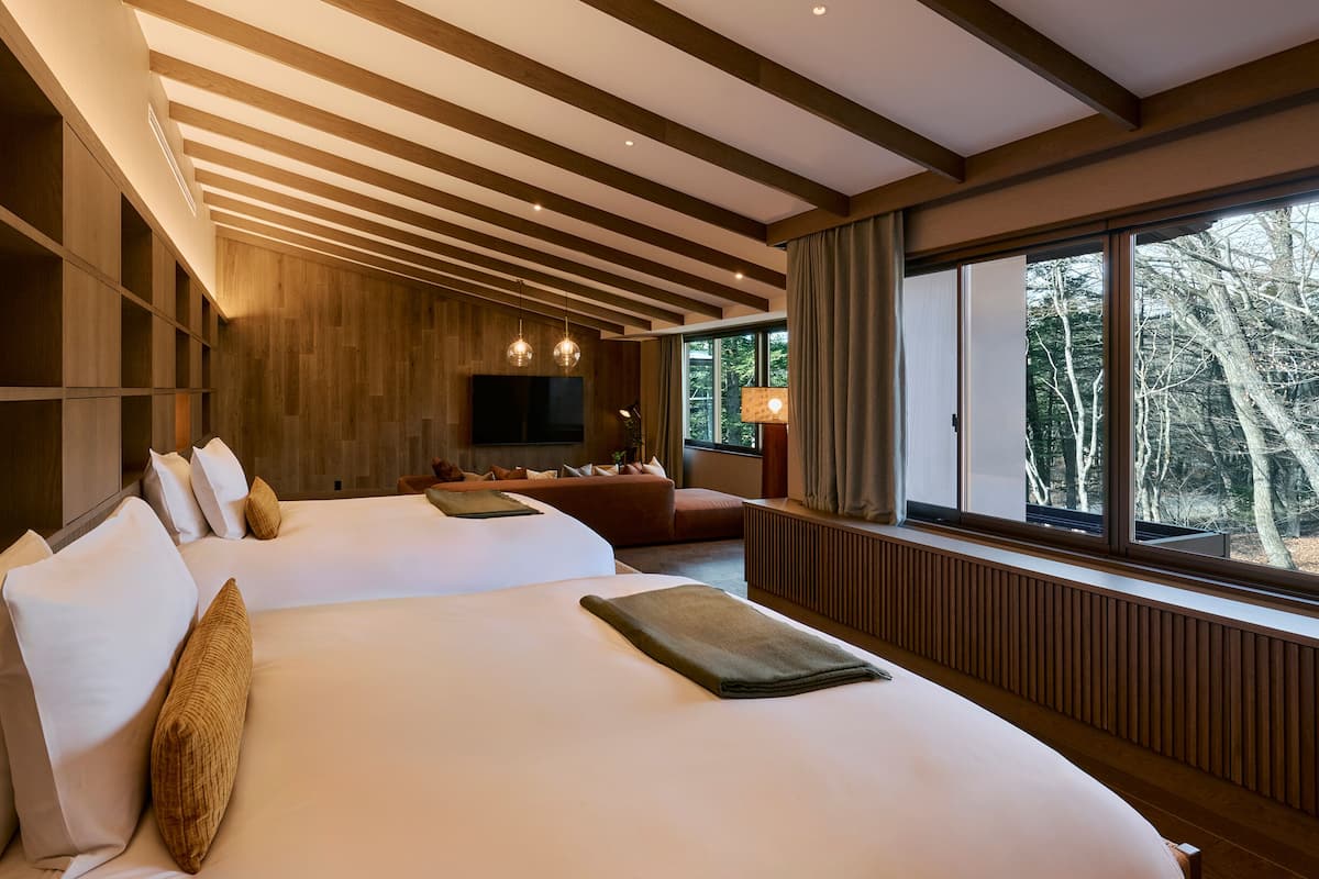 Ett modernt hotellrum med en stor säng, en soffa, en TV och ett fönster med utsikt över träd.