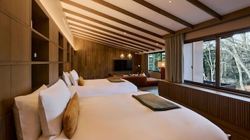 Quarto de hotel moderno com uma cama grande, um sofá, uma TV e uma janela com vista para árvores.