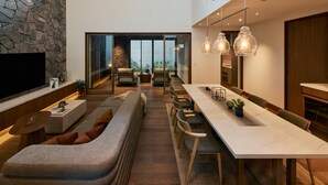 A modern interior with a long dining table, a sofa, and a TV mounted on the wall. - GLAMDAY STYLE HOTEL SUITE YAMANOFUMOTO (Karuizawa)