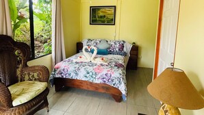 Une chambre à coucher avec un lit, un ventilateur de plafond, une chaise, une lampe et une fenêtre avec des rideaux.