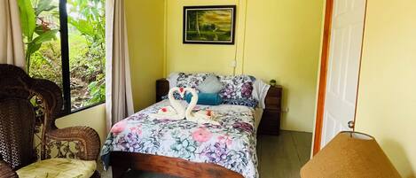 A bedroom with a bed, a ceiling fan, a chair, a lamp, and a window with curtains.