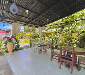 Ein Terrassenbereich mit gefliestem Boden, weißen Korbstühlen und einem Holztisch.