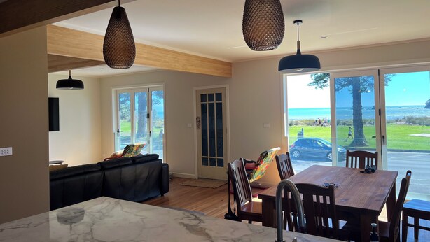 A modern kitchen with a marble countertop, a dining area with wooden chairs, and a view of the sea through large glass doors.