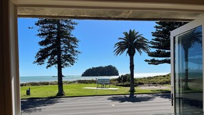 A view from inside a building looking out to a parking area with a road, grassy areas, and a beach with palm trees and a sign.