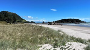A beach with a clear sky, grassy dunes, and rocky outcrops.