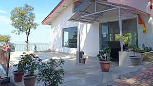 A modern house with a covered patio, potted plants, and a clear blue sky. - Barowalia Villa (Dalhousie)