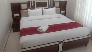 A neatly made bed with a white and red bedspread, wooden headboard, and bedside tables with lamps. - Barowalia Villa (Dalhousie)