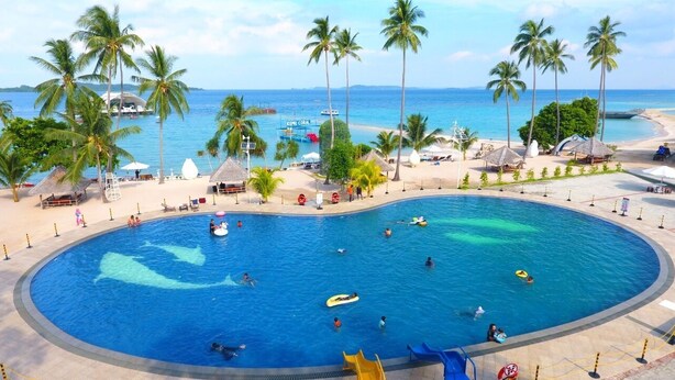 A large swimming pool with palm trees and beach views. - Kepri Coral Resort (Galang)