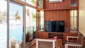 A wooden entertainment area with a flat-screen TV, glass doors leading to a pool, and a bench. - Kepri Coral Resort (Galang)
