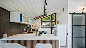 A modern kitchen with a central island, two grey upholstered chairs, a stainless steel refrigerator, and a sliding door closet.