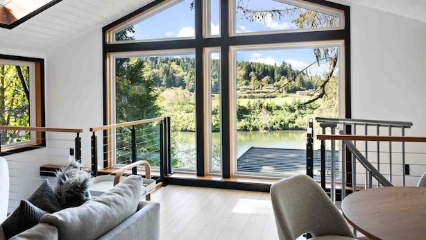 A modern interior with large windows offering a view of a lake and forest.