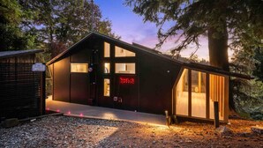 A cabin with a large window, a door with a red sign, and a gravel driveway.