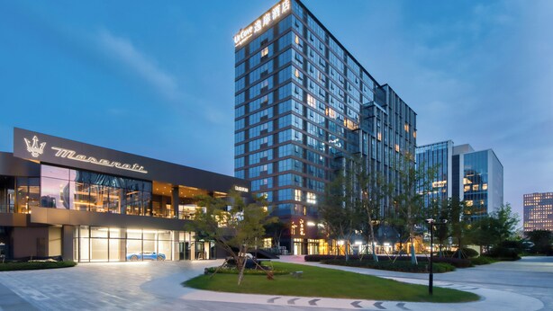 A modern hotel with a glass facade, a visible car in the entrance, and a well-lit exterior. - UrCove by Hyatt Hangzhou North Grand Canal (Hangzhou)
