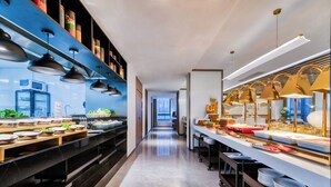 A modern kitchen with stainless steel appliances, a long counter with food items, and pendant lighting. - UrCove by Hyatt Hangzhou North Grand Canal (Hangzhou)