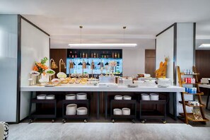 A modern hotel lobby with a long reception desk, shelves with various items, and a decorative plant arrangement. - UrCove by Hyatt Hangzhou North Grand Canal (Hangzhou)