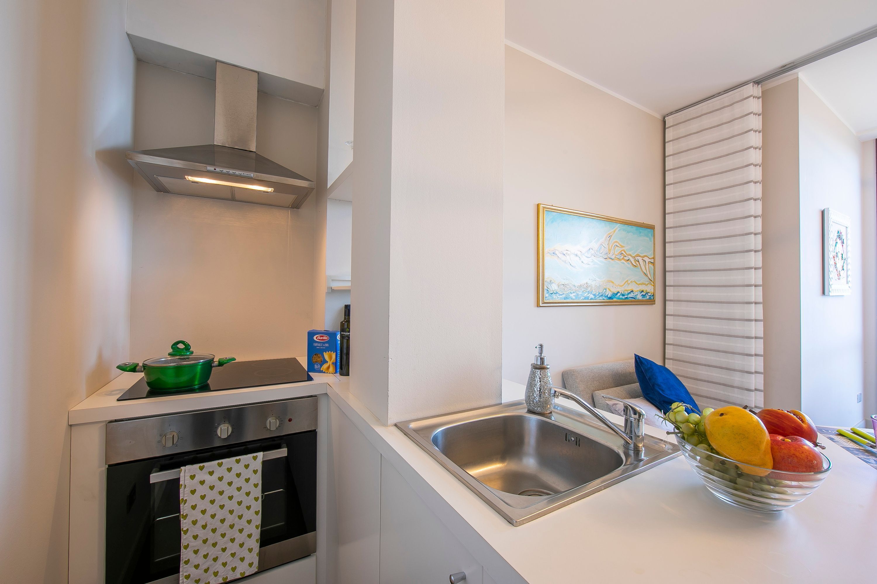 A modern kitchen with a stainless steel range hood, a built-in oven, a sink, and a bowl of fruit on the counter.