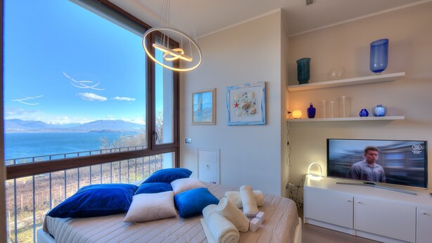 Un dormitori modern amb un llit gran, televisió i un balcó amb vista al mar.