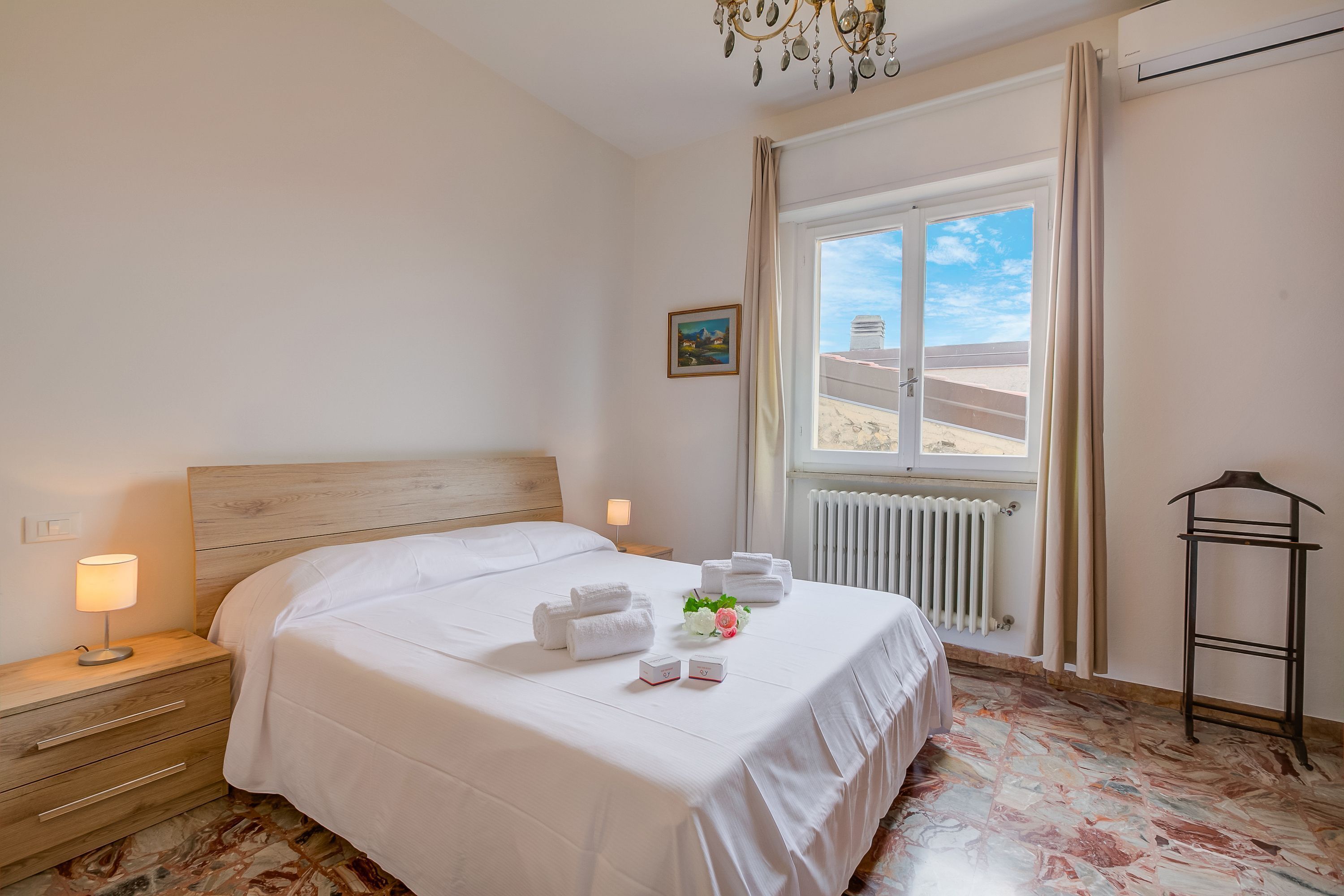 Ein Hotelzimmer mit einem großen Bett, einem Nachttisch mit Lampe, einem Heizkörper und einem Fenster mit Vorhängen.