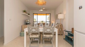 A dining area with a white table, two grey chairs, a ceiling fan, and a window with an orange curtain. - Ventana A Do ana in Sanlucar de Barrameda (Sanlucar de Barrameda)