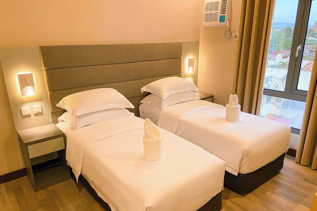 A hotel room with two beds, a nightstand, and a window with curtains.