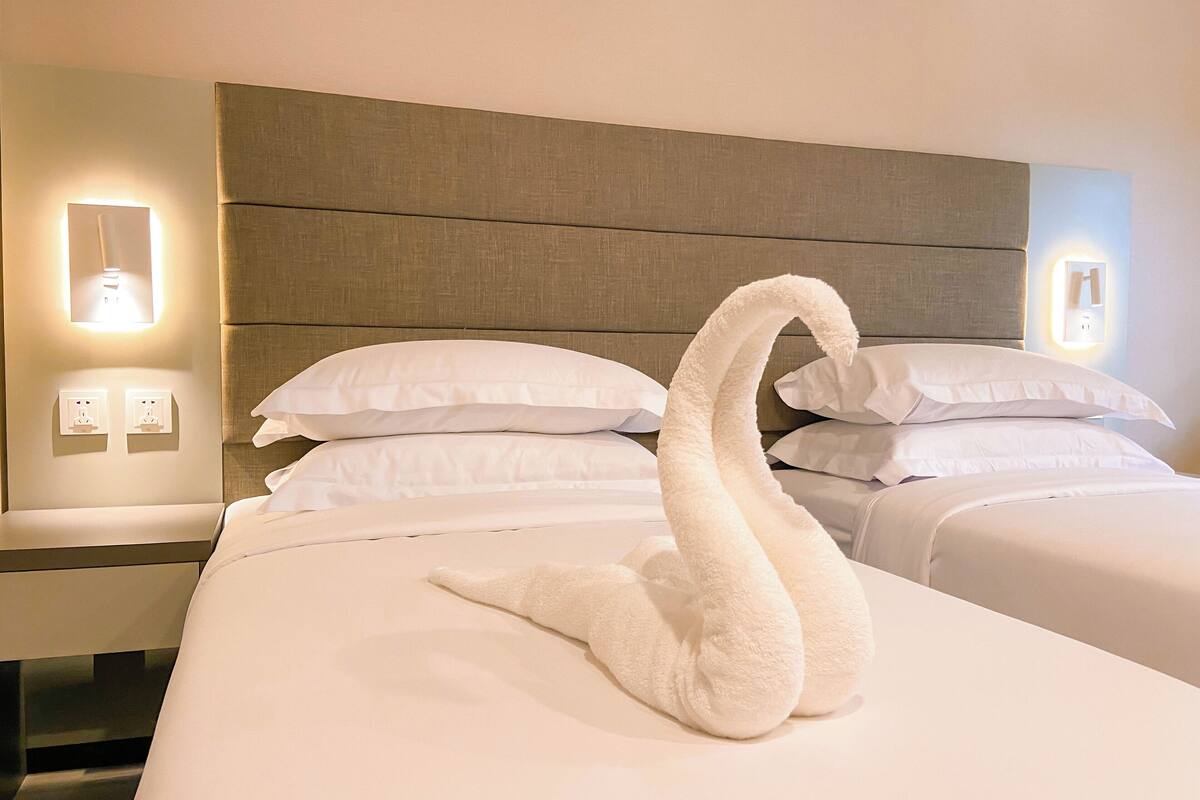 A hotel room with a neatly made bed, two pillows, and a swan-shaped towel centerpiece.