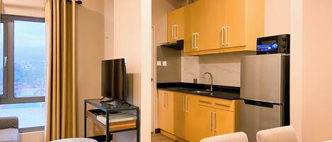 A modern kitchen with yellow cabinets, a black refrigerator, and a built-in microwave. There is a small dining area with a white table and two chairs.