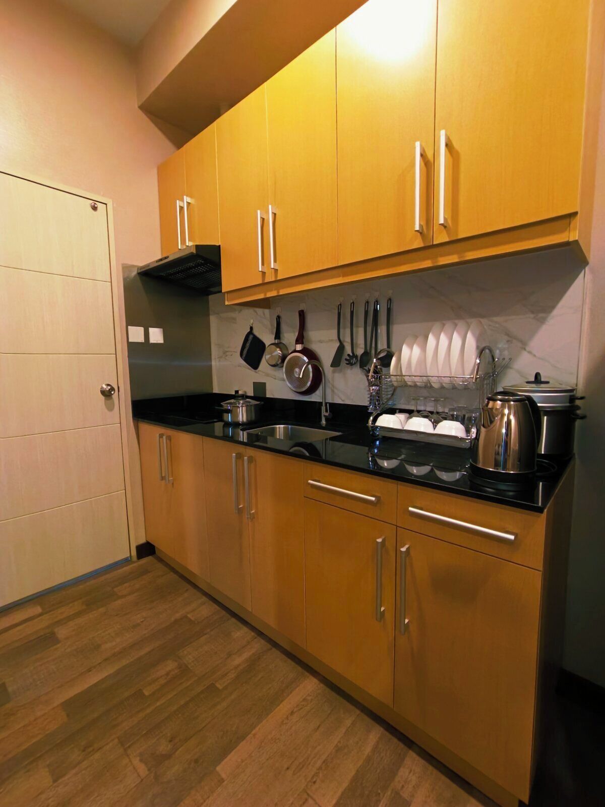 Una cocina con armarios de madera, encimera negra y diversos utensilios de cocina colgados en la pared.