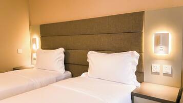 A hotel room with two single beds, a headboard, bedside lamps, and a nightstand with a lamp.
