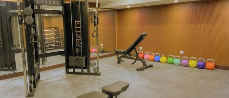 A gym with weight machines, a bench, and colorful kettlebells.