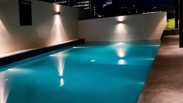 A swimming pool with a tiled floor and walls, surrounded by walls with recessed lighting.