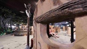 An indoor setting with a rustic, naturalistic design, featuring stone walls and wooden structures. - Knight's Hotel Europark Resort (Qihe County)