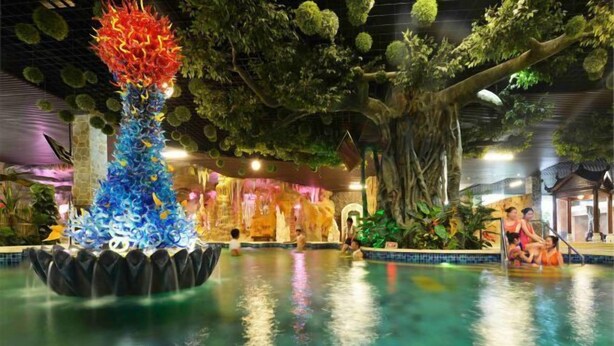 An indoor pool area with a decorative fountain, lush artificial greenery, and a seating area with people. - Knight's Hotel Europark Resort (Qihe County)