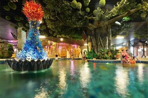 An indoor pool area with a decorative fountain, lush artificial greenery, and a seating area with people. - Knight's Hotel Europark Resort (Qihe County)