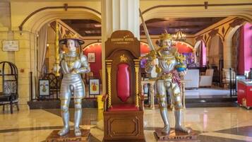 Two statues of armored figures in a lobby with a grand chandelier and a red cushioned seat.