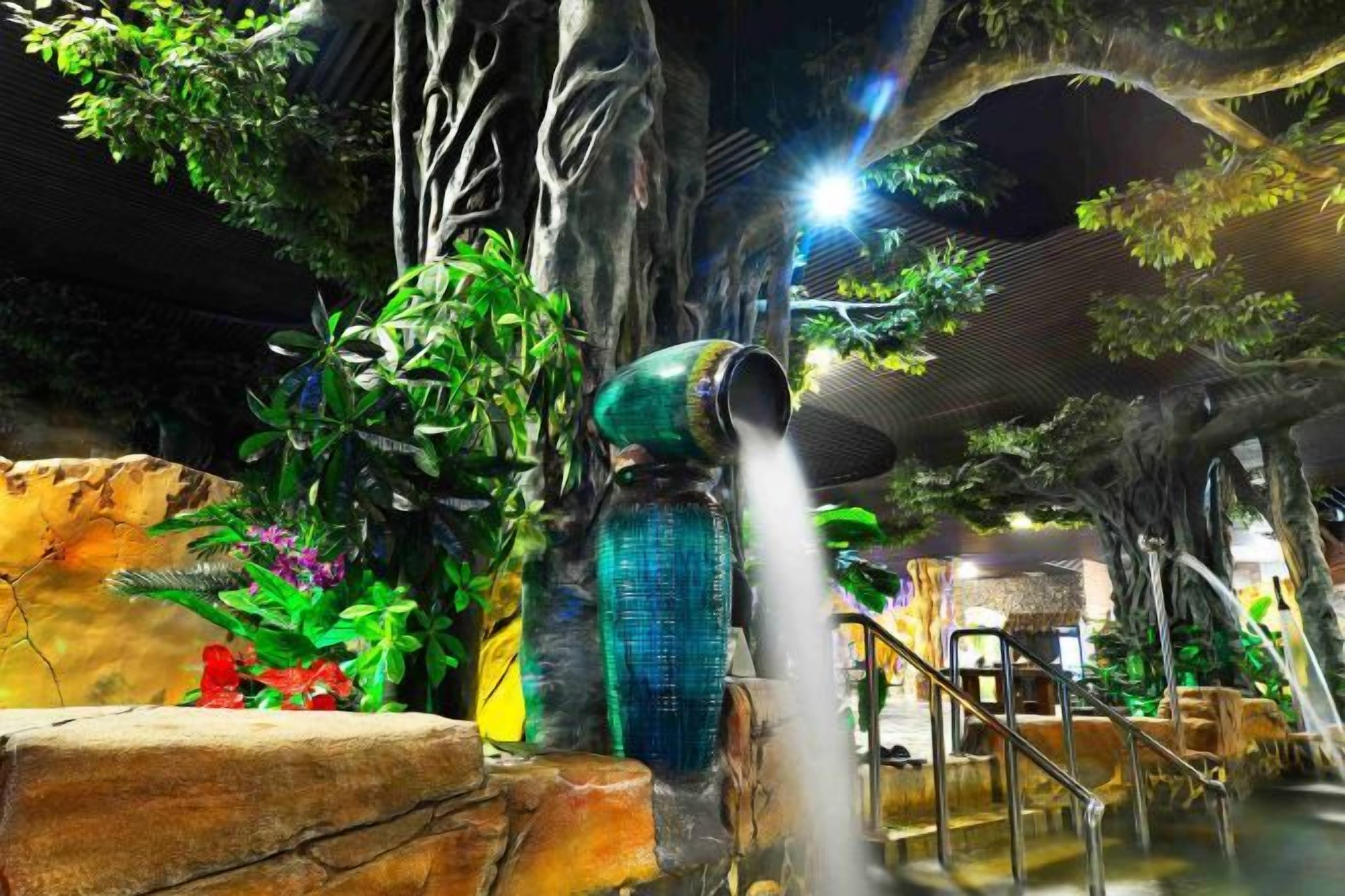 Uma fonte de água em ambiente interno, rodeada por plantas e uma parede de pedra.