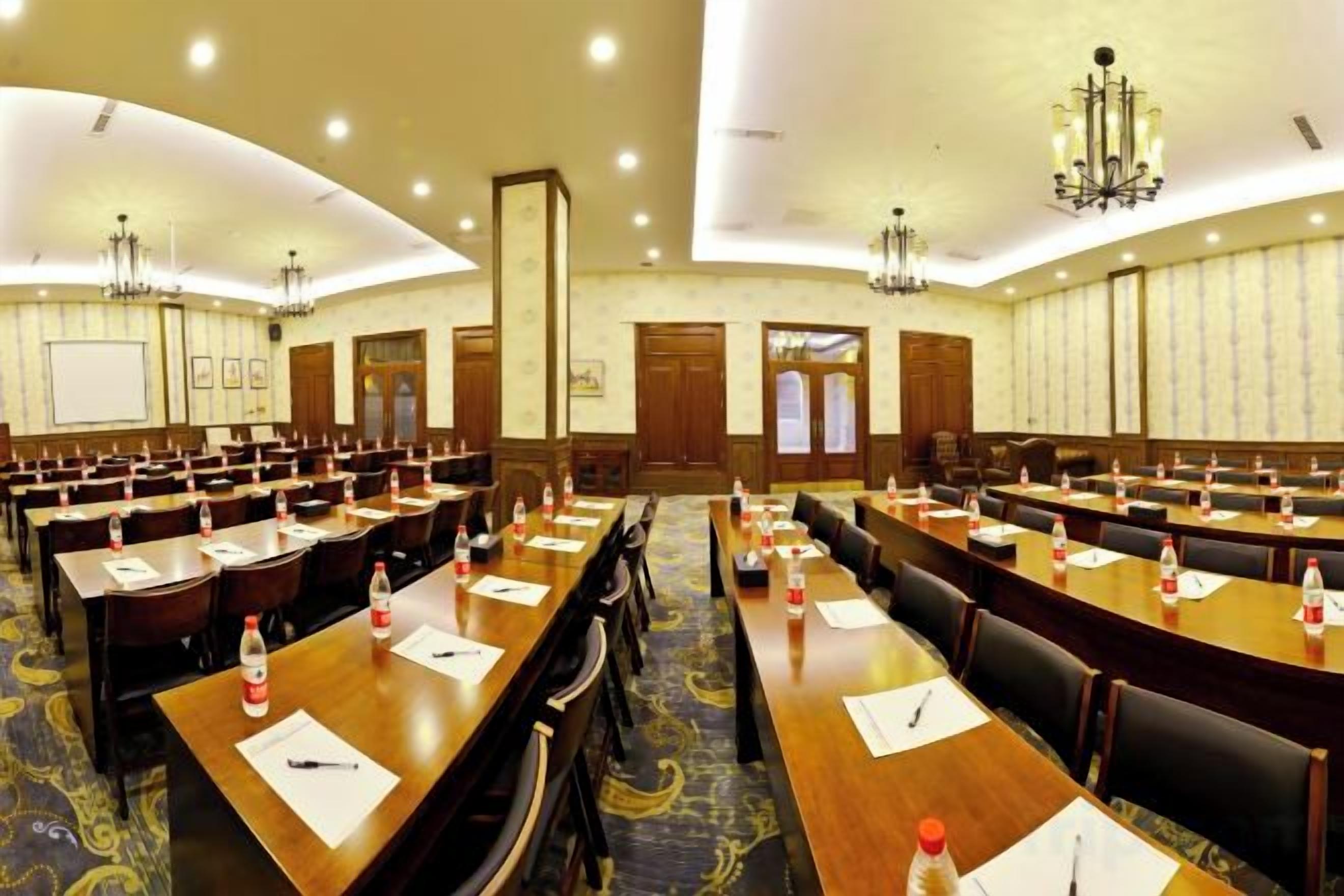 A conference room with multiple tables and chairs, equipped with water bottles and notepads.