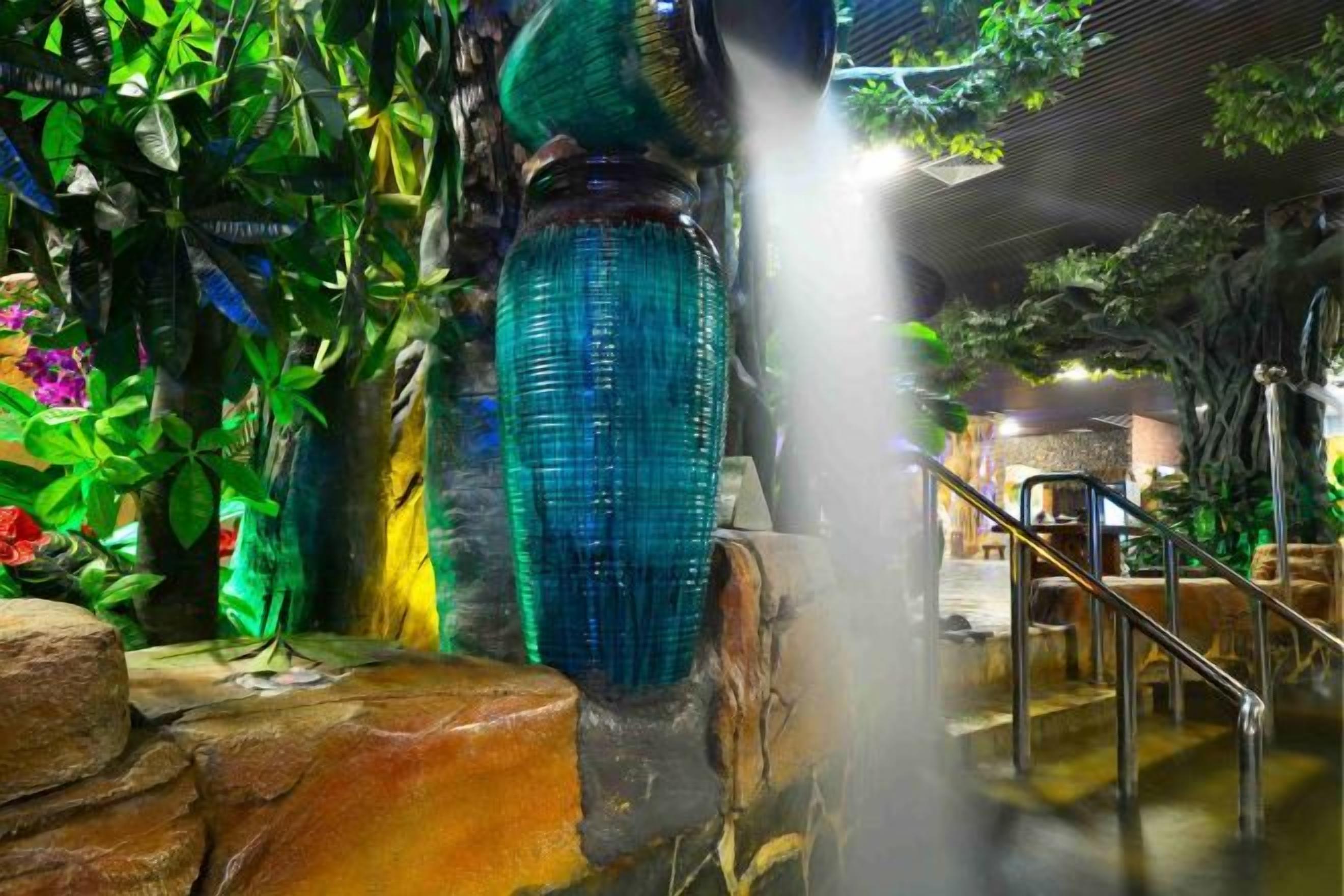 A water feature with a blue glass structure, surrounded by lush greenery and a stone base.