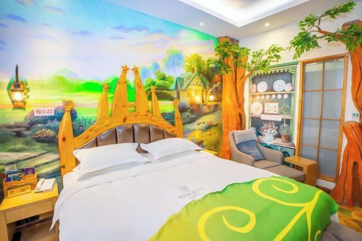 Une chambre à coucher avec une fresque représentant un paysage de village, un cadre de lit en bois, une table de chevet, une chaise et une fenêtre avec des rideaux.