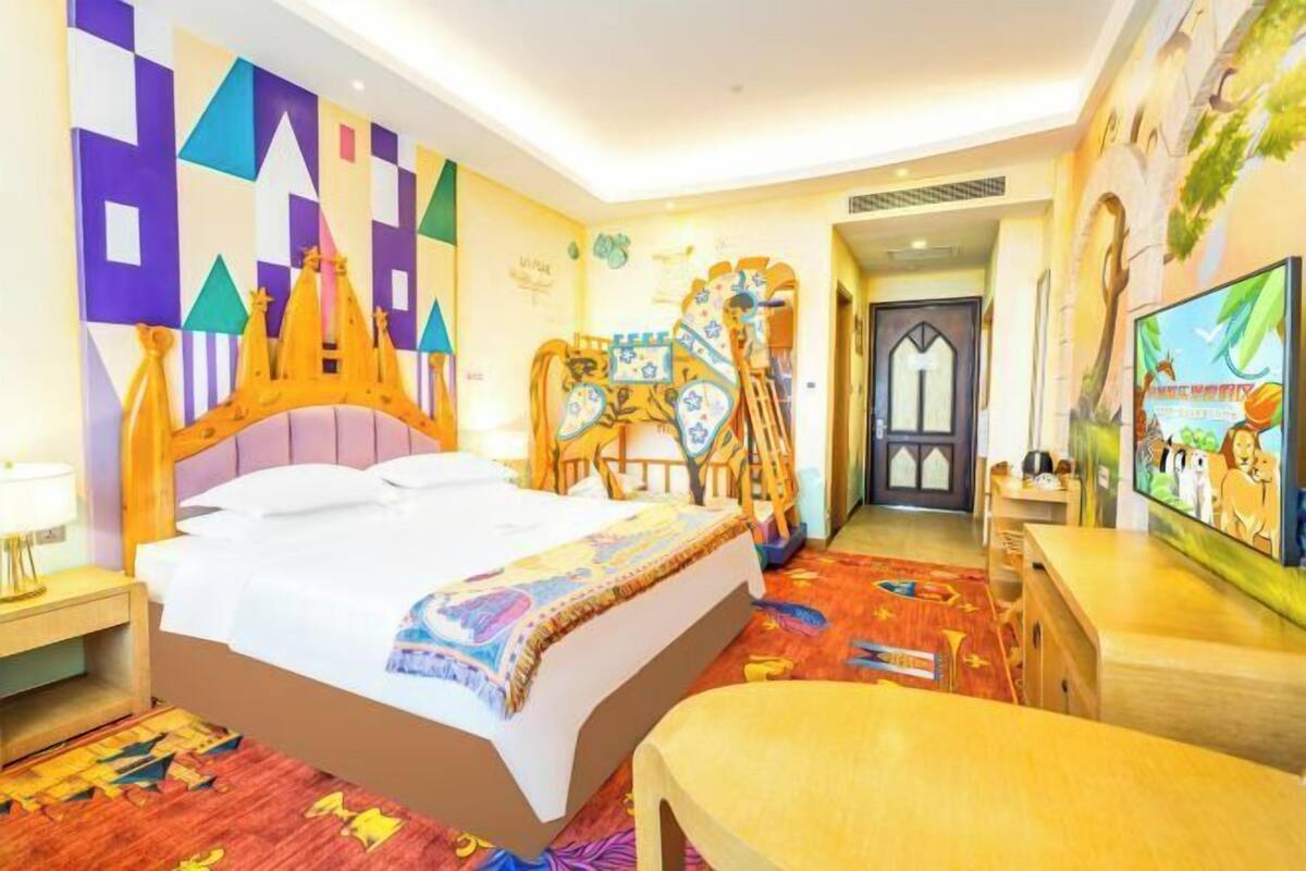Une chambre d’hôtel avec un grand lit, une tête de lit en bois, un tapis coloré, une télévision et une porte donnant sur une autre pièce.