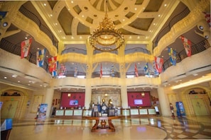 A spacious lobby with a central chandelier, multiple levels with balconies, and a check-in counter.