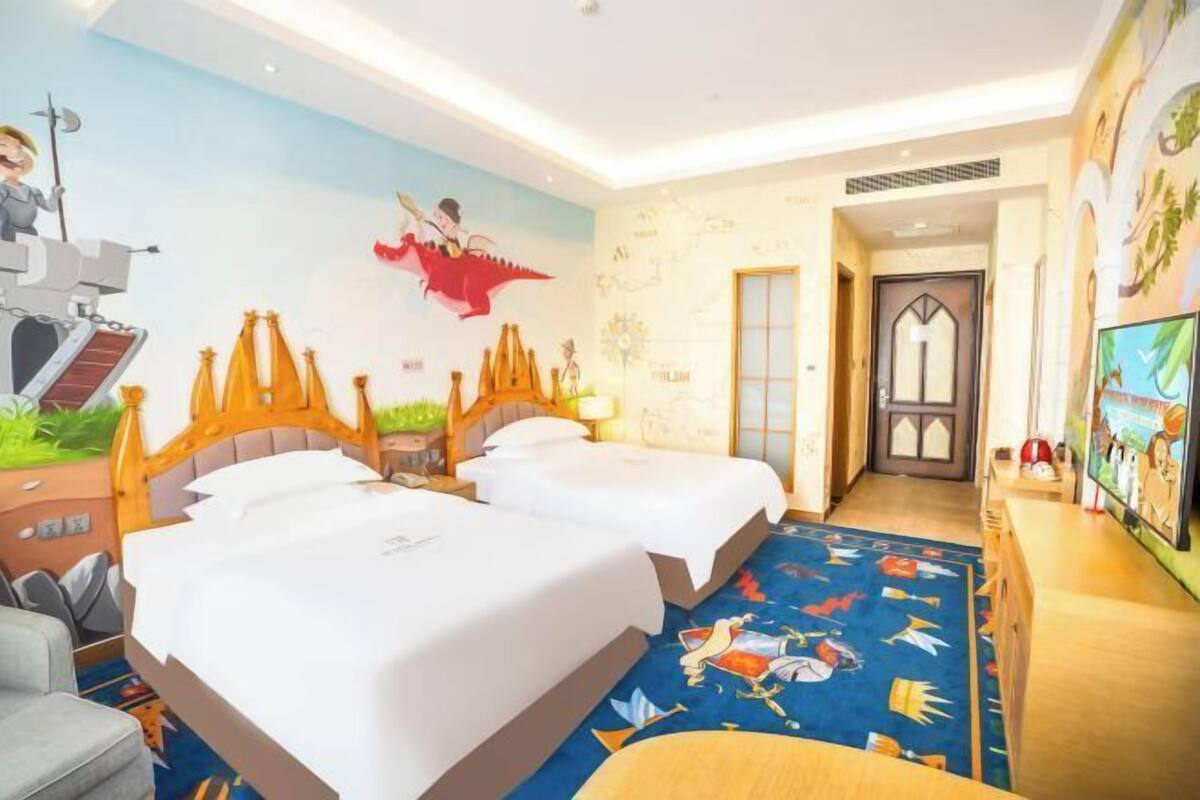 Une chambre d’hôtel avec deux lits, une fresque murale et un téléviseur placé à droite.