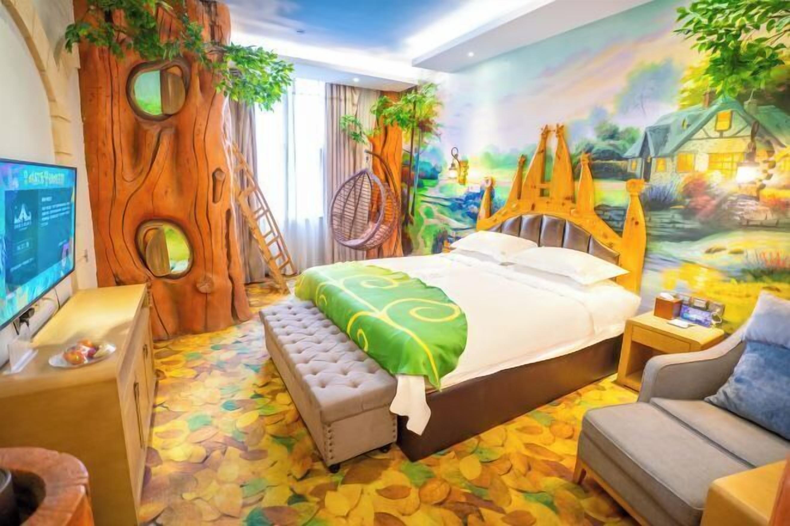 A bedroom with a bed, a chair, a bench, a TV, and a mural of a tree and landscape.