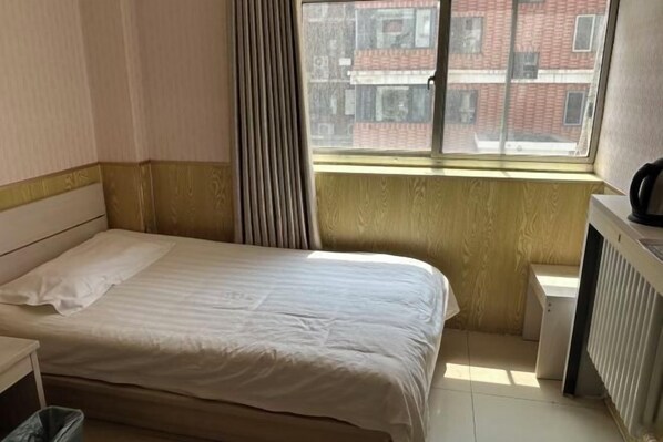 A small, neatly arranged bedroom with a single bed, a radiator, and a window with a view of buildings outside. - Beijing Yixin Express Hotel (Miyun Great Wall Huandao Branch) (Beijing)