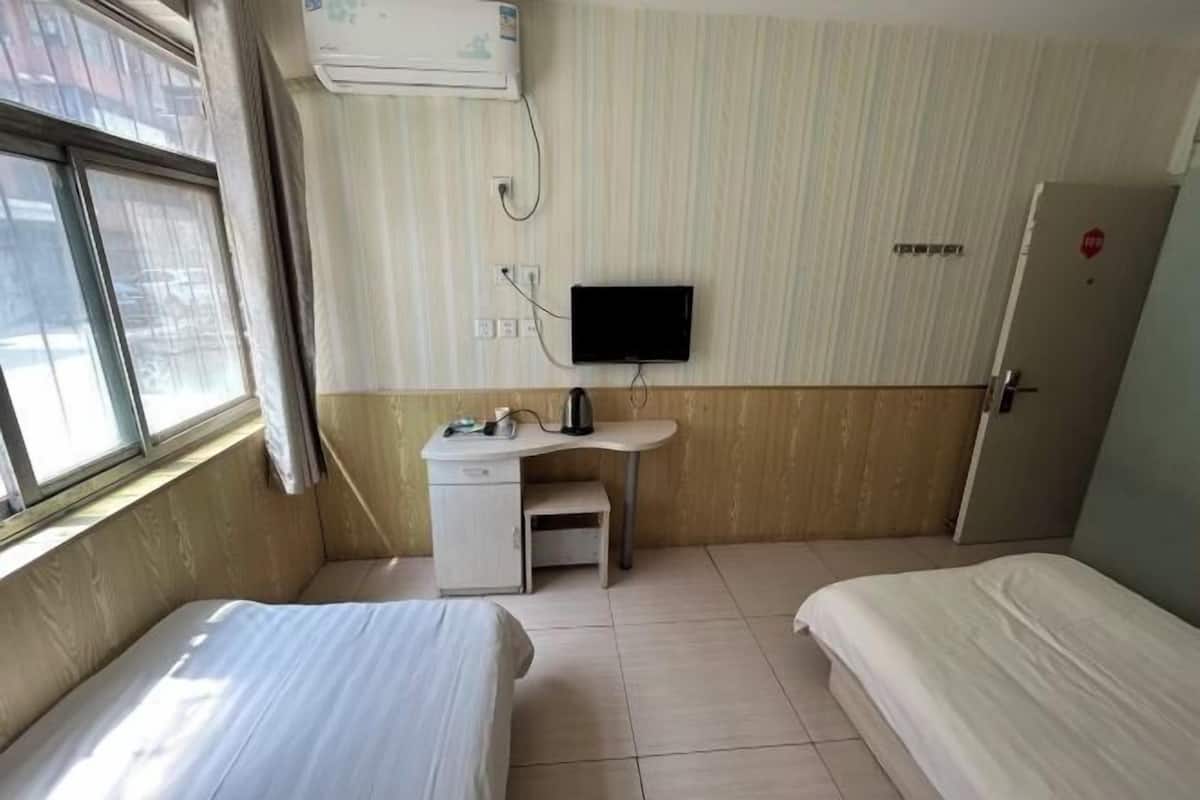 A hotel room with two beds, a desk with a television, and an air conditioning unit.