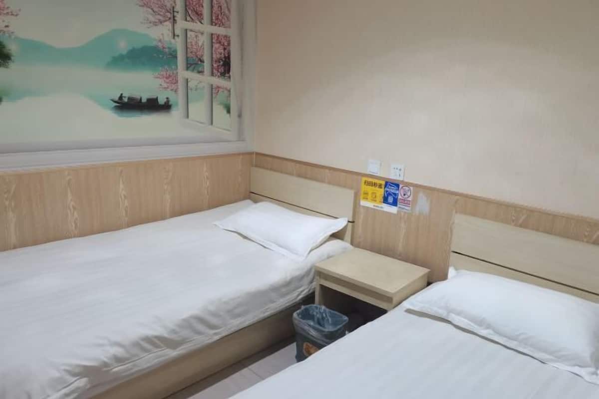 A room with two single beds, a small bedside table, a trash bin, and a window with a painting of a boat on water.