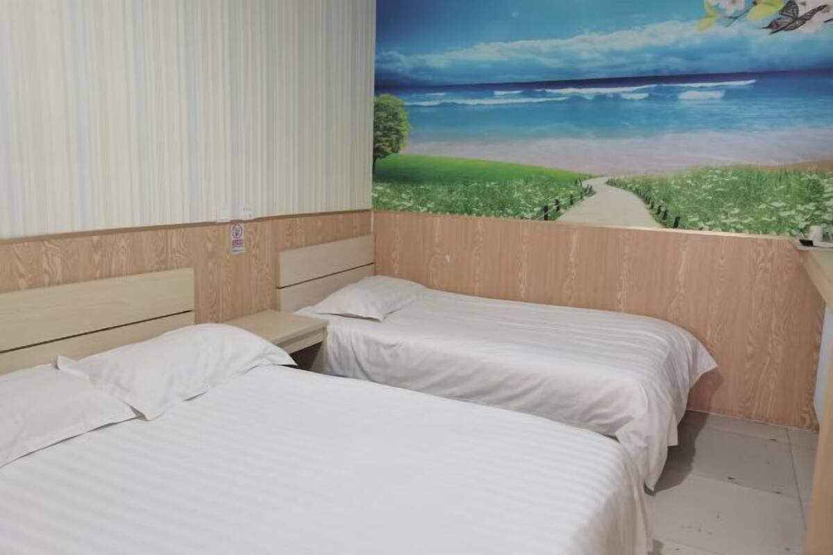 A bedroom with two beds, a wooden headboard, a nightstand, and a mural of a beach scene.