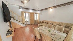 Amplia sala de estar con una mesa de comedor lista para cuatro personas, un sofá y una escalera que conduce a otra habitación.