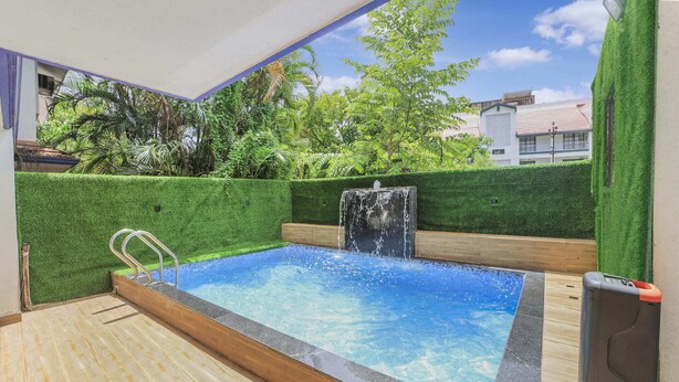 Una piscina con cascada, rodeada de setos verdes y una terraza de madera.
