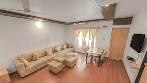 Un amplio salón con un sofá beige grande, una mesa de centro de vidrio y una mesa de comedor con sillas.