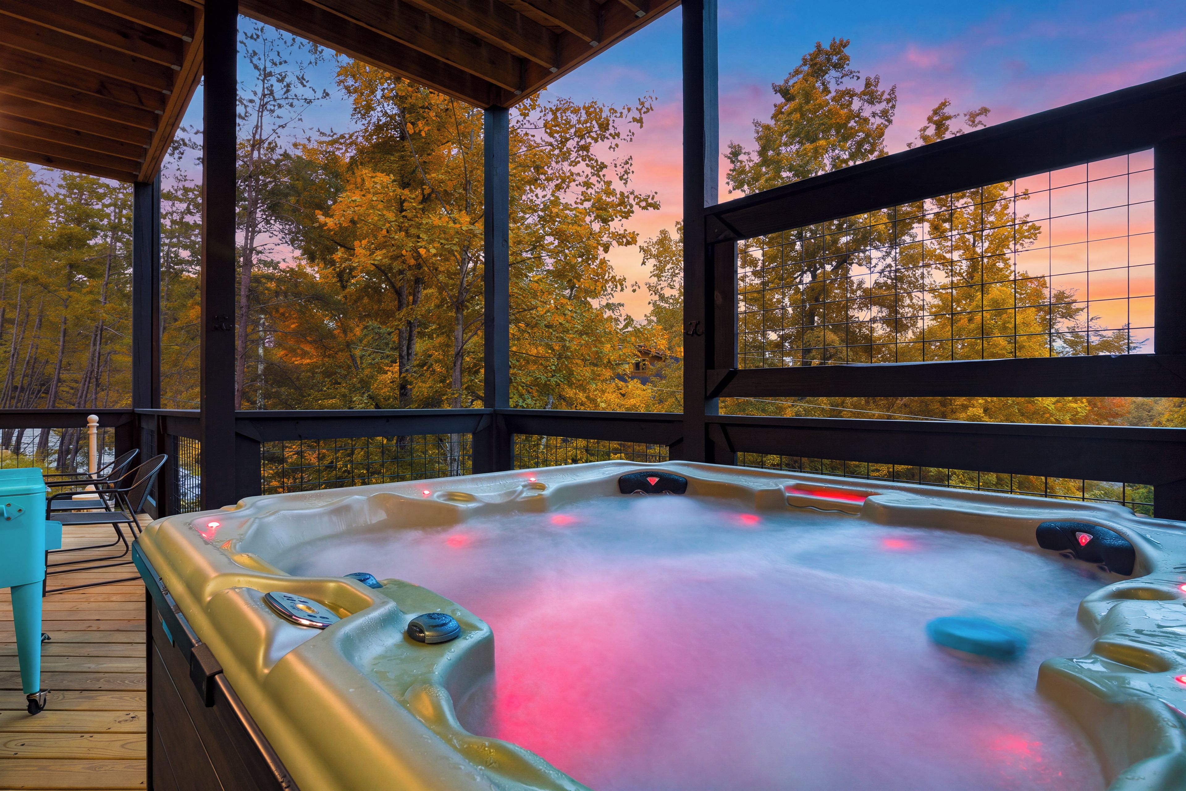 A hot tub on a wooden deck with a view of autumn trees and a sunset.